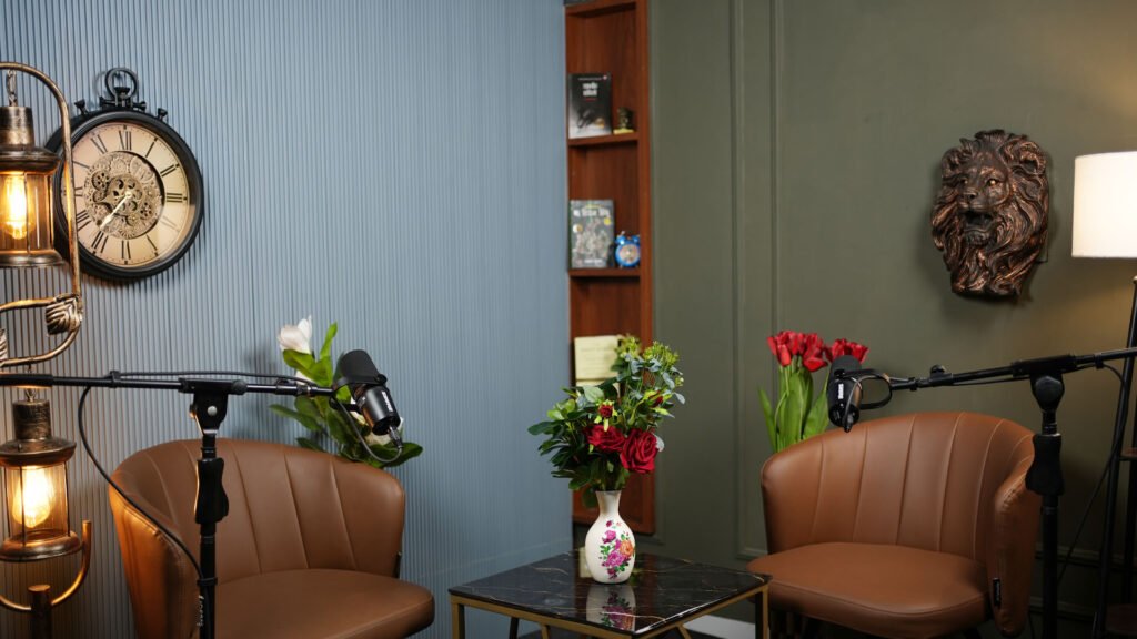 Light grey themed podcast set with armchairs, flowers and microphone arms
