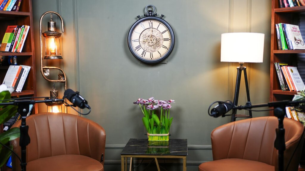 Wall clock, armchairs and fresh flowers in the grey themed podcast set