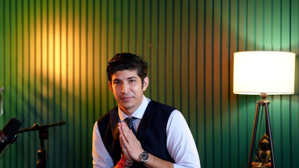 Guest smiling with folded hands in front of a green slatted wall at Oskillo Studio